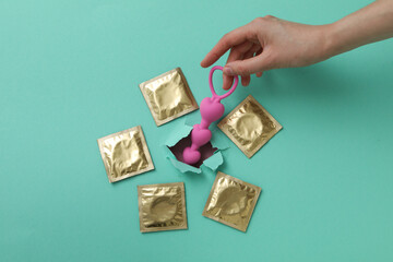Pink anal balls with condoms on a background of torn turquoise paper
