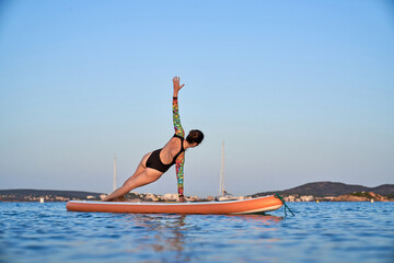 Unrecognizable woman practicing yoga in Side Plank on paddleboar