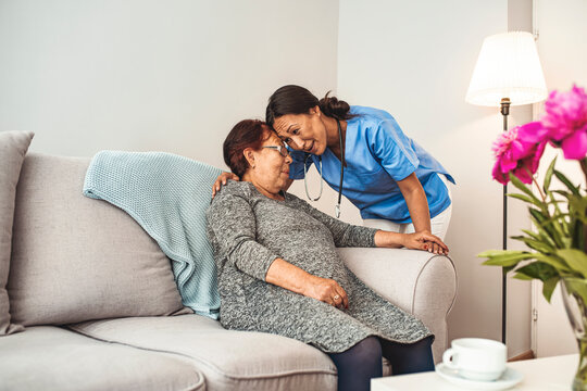 Nurse Making Home Visit To Senior Woman. Friendly nurse supporting an eldery lady. Female home caregiver talking with senior woman, sitting in living room and listening to her carefully.
