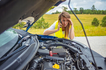 Fototapeta na wymiar Photo of a Caucasian woman using a smartphone in front of her broken car on the road. Contacting car technician or need help concept. A young sad woman calling a car repair service with her phone