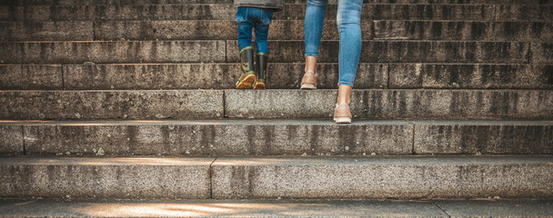 Mother walking with her son at the park at sunset. Mother teaching her boy to climb stairs. Unrecognisable mother helps her son climb up the stairs. Mother and her son, Baner concept