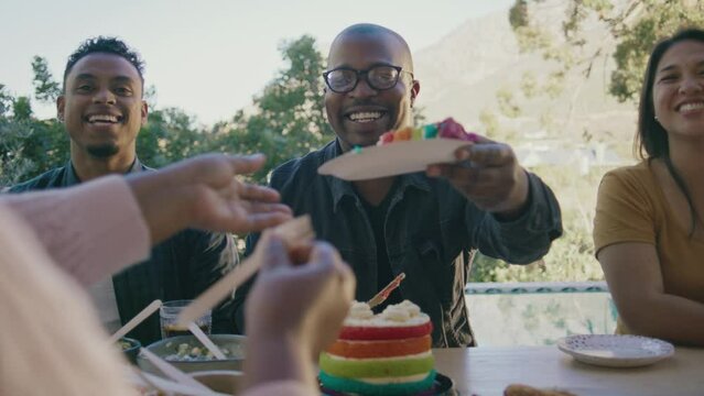A Man Cutting and Passing Out Rainbow Birthday Cake with Friends