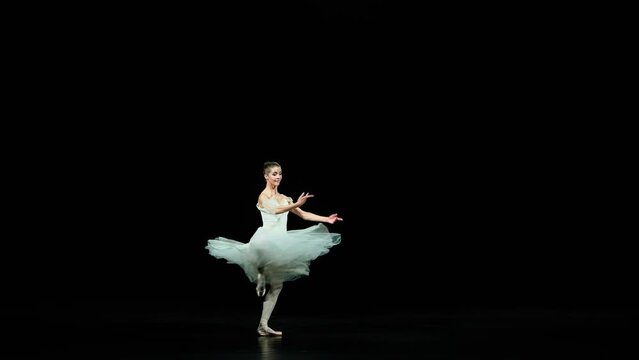 Slow motion, graceful ballerina in a white dress dance and perform choreographic elements on a black background, beautiful dramatic dance with pirouettes.