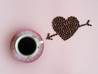 Creative layout made of pink floral coffee cup and heart and arrow made of coffee beans against pastel pink background. Flat lay, copy space. Love design. 
