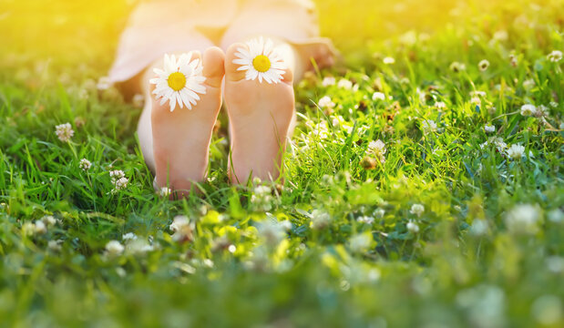 Little girl  barefoot sits on the grass in  summer park.