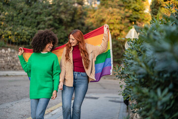 two gay multiracial lesbian women with rainbow flag gay pride day through the city streets