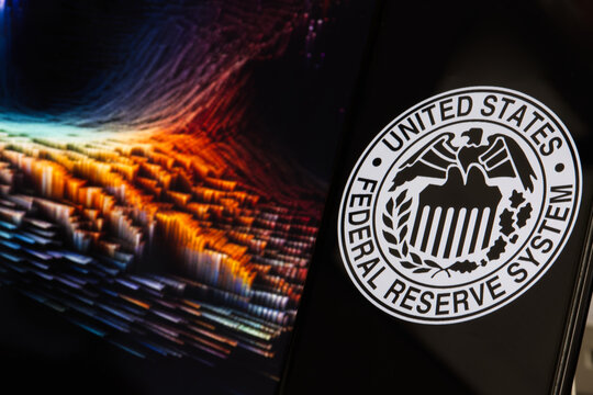 Smartphone with Federal Reserve (FED) symbol against a background of fluctuating market charts, blurred, USA, August 16, 2023