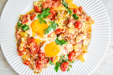 Shakshouka for breakfast. Homemade shakshuka, fried eggs, onion, bell pepper, tomatoes and parsley in a pan. Marble background. Top view. chakchouka