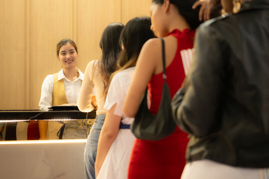 Young asian woman standing in line to buy movie tickets and in hand popcorn and drink, Smiling ticket salesman serving.