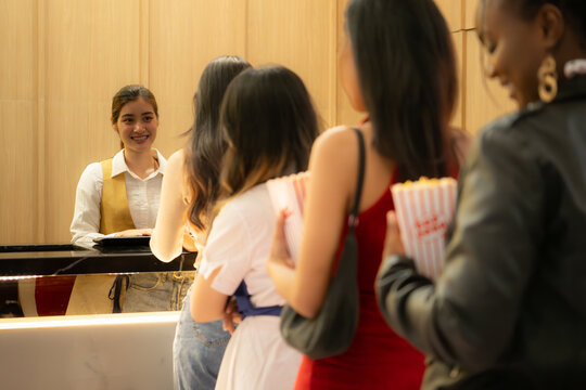 Young asian woman standing in line to buy movie tickets and in hand popcorn and drink, Smiling ticket salesman serving.