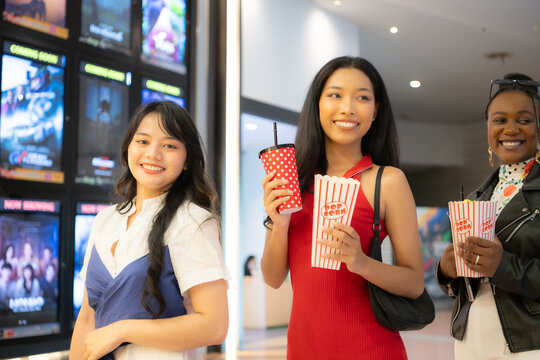 Young asian woman standing in line to buy movie tickets and in hand popcorn and drink