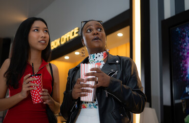 Both of young woman stand and watch the movie program to watch today.