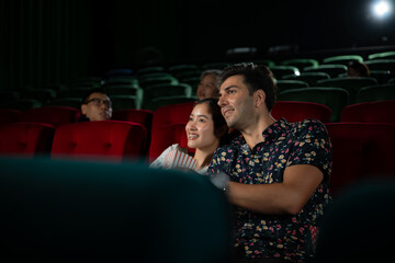 Young man and woman watching movie in cinema, sitting on red seats