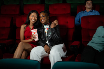 Both of young woman watching movie in cinema, sitting on red seats