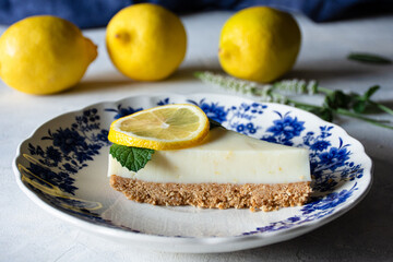 primer plano de una tarta de limón y galleta sobre un plato decorativo en una mesa, con limones al...