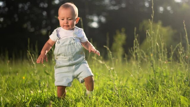baby falls into the grass learns to walk in the park. happy family kid dream concept. baby takes the first steps unsuccessfully falls in nature in the summer in the park lifestyle