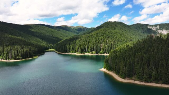 Aerial view of blue lake and green forests. Mountain forest lake with pine trees. View on the lake between mountain forest. Over crystal clear mountain lake water. Fresh water. Glacier turquoise water