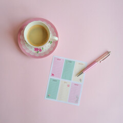 Creative layout made of pink floral coffee cup, colorful planner and rose gold pen against pink background. Flat lay, copy space. Morning routine. Girly essentials. 