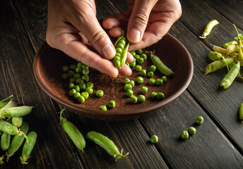 Man's hands clean green peas from pods. Work environment on the kitchen table. Copy space