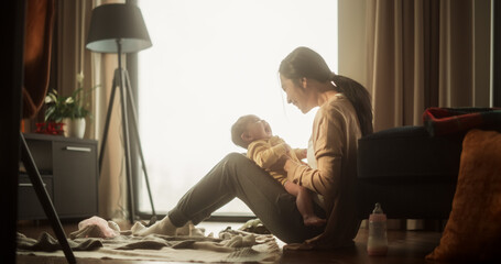 Mother and Baby Bonding Moment: Authentic Shot of an Asian Woman New to Motherhood Playing with her Cute Child in the Morning at Home. Cozy and Warm Atmosphere for a Mother and her Infant - obrazy, fototapety, plakaty