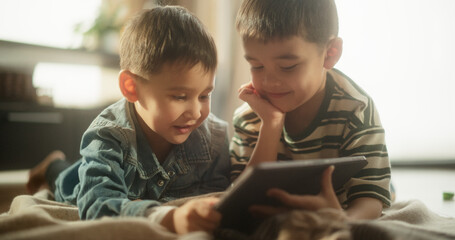 Portrait of Two Male Asian Kids Using a Digital Tablet During Weekend in their Room. Two Cute Siblings Watching Educational Content Online, Sharing the Gadget, and Enjoying their Time