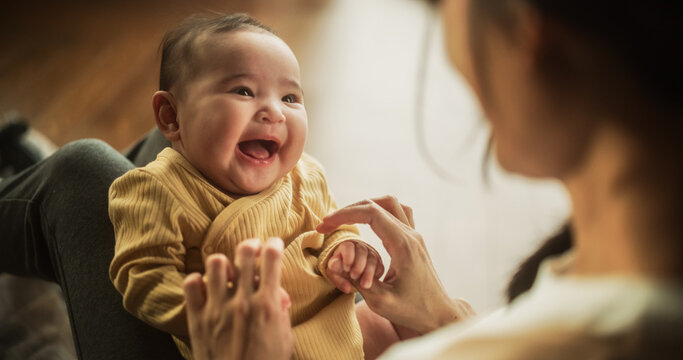 Portrait of a Cute Asian Baby Laughing, Resting on Her Mother's Lap and Enjoying a Bonding Time Together, Looking at her with Love. Playful Mom Tickeling her Toddler and Playing with Her.