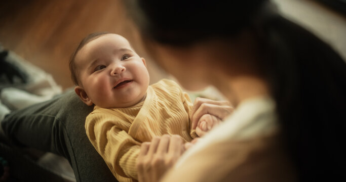 Portrait of a Cute Asian Baby Laughing, Resting on Her Mother's Lap and Enjoying a Bonding Time Together, Looking at her with Love. Playful Mom Tickeling her Toddler and Playing with Her
