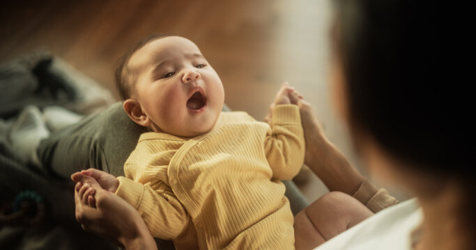 Portrait of a Cute Asian Baby Laughing, Resting on His Mother's Lap and Enjoying a Bonding Time Together, Looking at her with Love. Playful Mom Tickeling her Toddler and Playing with Him
