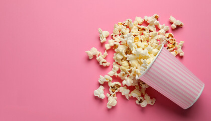 Overturned paper cup with delicious popcorn on pink background, flat lay. Space for text