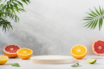 Empty wooden round podium on light grey background surrounded by citrus fruits. Display, pedestal for the presentation of cosmetic products, drinks - obrazy, fototapety, plakaty
