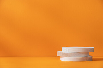 Wooden cylindrical podiums stack on orange background with copy space. Podium, display for the presentation of goods