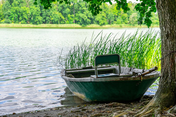 Naklejka na ściany i meble The rowing fishing boat in the foreground moored under a chestnut tree on the shore.