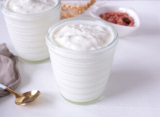 Greek yogurt in cup glass and brown cloth, spoon, granola on white wooden background.