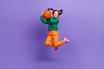 Full length photo of excited funky small girl wear green sweatshirt jumping high rising basketball...