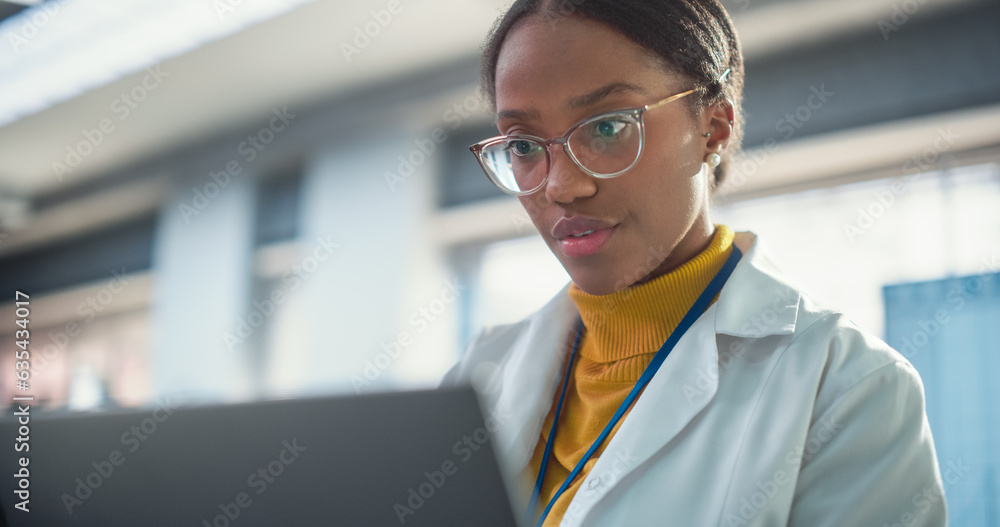 Leinwandbilder portrait of young black female expert in a lab coat smiling and using laptop computer. professional 