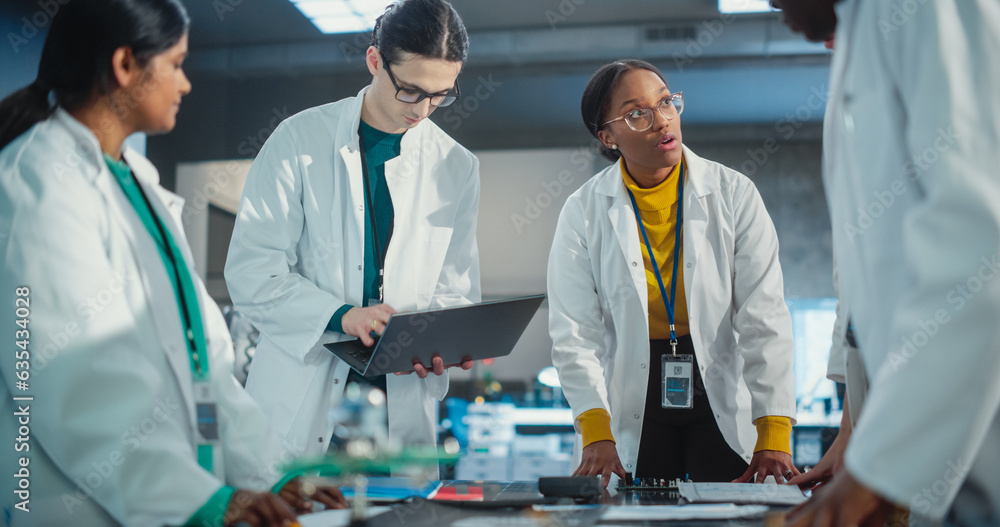 Poster Diverse Team of Industrial Robotics Specialists Gathered Around a Table to Discuss a Blueprint. Engineers In Lab Coats Using Laptop and Tablet, Brainstorming Ideas For Electronic Components