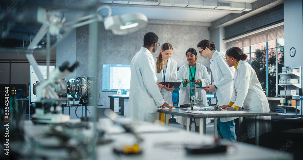 Fototapete Group of International Multiethnic Lab Specialists Gathering Around a Table to Discuss Blueprints and Components for a High Tech Robotic Project. Young Engineers Working in Company Facility Laboratory