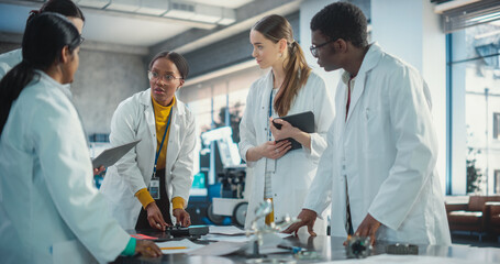 Group of Young Professional Specialists Brainstorming, Solving Problems Using Laptop and Tablet Computers. Manufacturing Project Managers Discussing Blueprint, Data Gathered in Product Analysis.