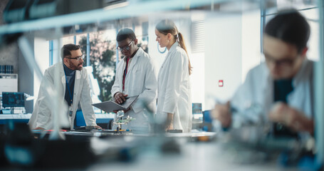 Diverse Young Group of Engineers Working in a Modern Startup Lab. Male Specialist Soldering a Circuit Board While Team of Professionals Discuss Technological Project Strategy Using Laptop Computer.