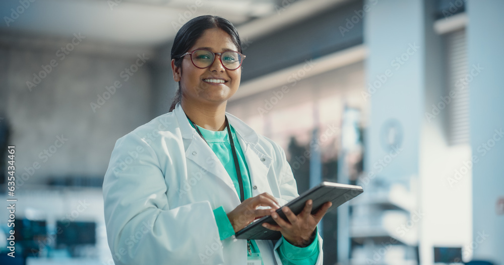 Leinwandbilder portrait of young indian female specialist in a lab coat smiling and using laptop computer. professi