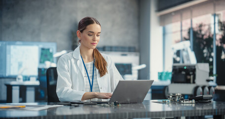 Portrait of Caucasian Young Female Scientist Using Laptop Computer, Working On Inventions in a Laboratory. Confident Professional Woman Working as Lead Engineer, Monitoring Technology Projects