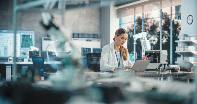 Portrait of Professional Female Scientist Working in Industrial Lab Using Laptop Computer. Successful Engineer Checking and Monitoring Production Quality, Analysing Data Using Advanced Technology