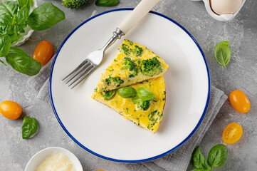 Omelette with broccoli, cheese and fresh basil on a plate on a gray concrete background. Healthy breakfast.