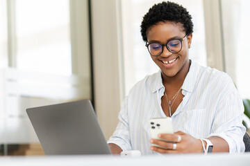 Determined African businesswoman, student, freelancer checking emails on the smartphone while using...