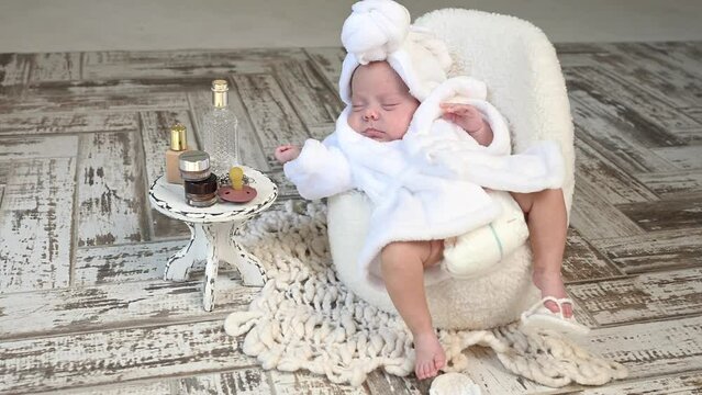 Sleeping newborn beautiful cute baby girl or boy during first week of life. 4k slow motion raw video. Happy Family morning concept. Small baby at white chair in white bathroom coat with towel on head 