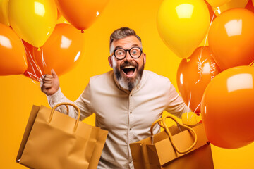 Portrait of wow excited amazed man with open mouth holding colored helium balloons and shopping bags on a yellow background