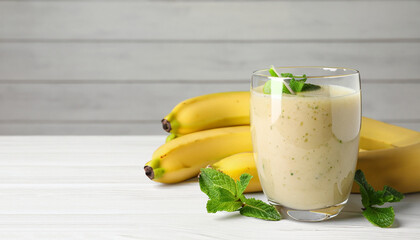 Glass of tasty smoothie, mint and fresh bananas on white wooden table, space for text. Banner design