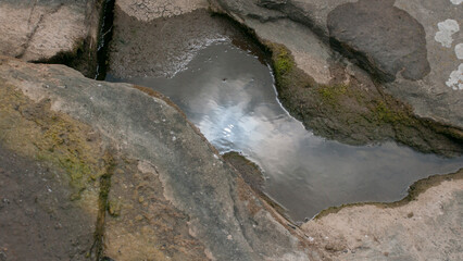 Reflejo del sol en agua estancada entre rocas