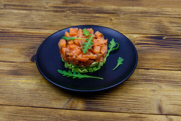 Salmon tartare with avocado and arugula on wooden table