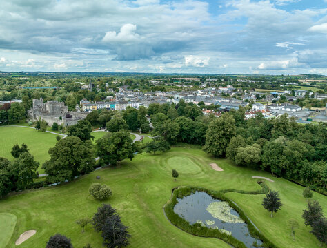 Aerial view of Cahir castle and town in Ireland with Tower House, outer castle, circular, rectangular towers, banquette hall, guarding the crossing on the River Suir with a waterfall and golf course